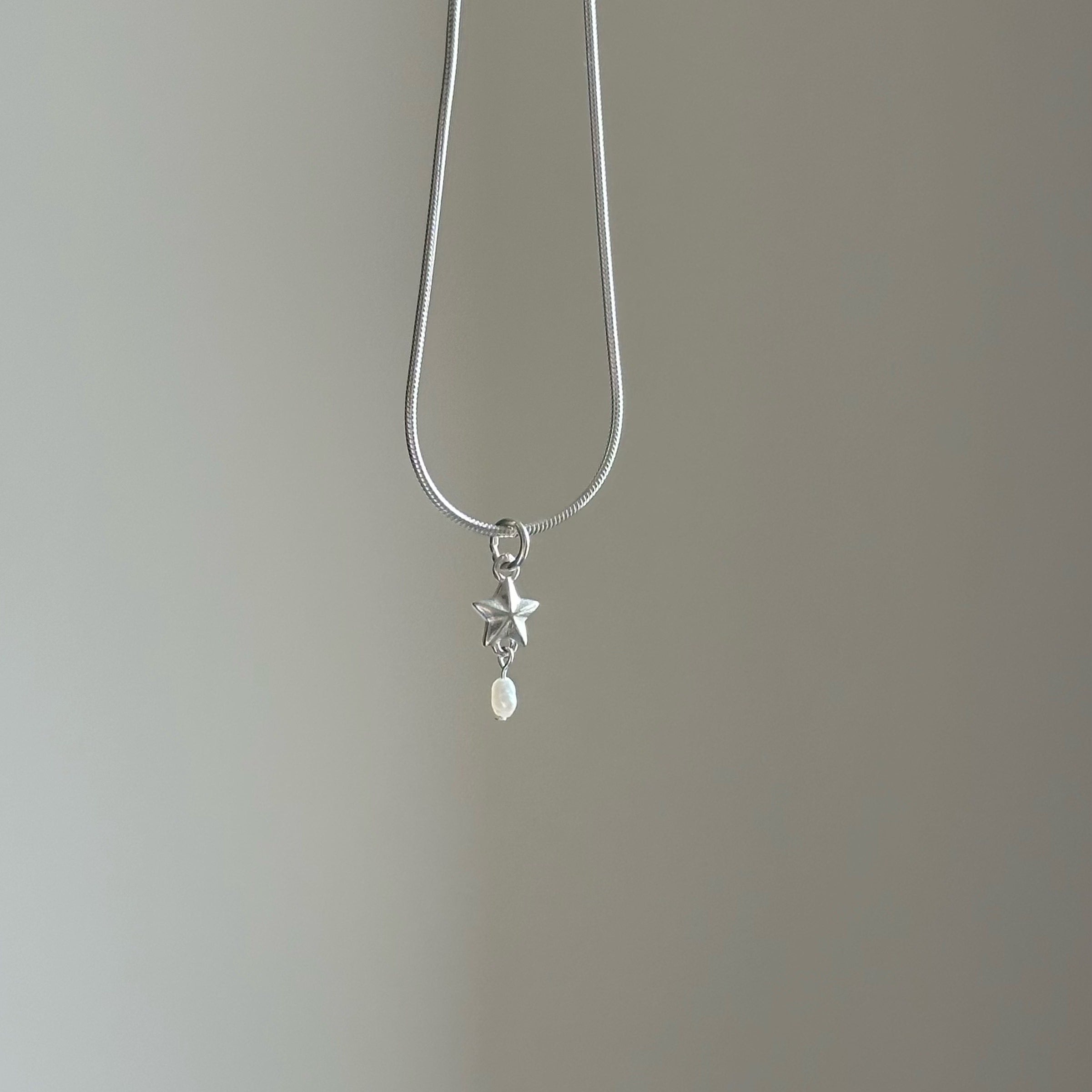 Silver necklace with a star and pearl pendant on a plain background