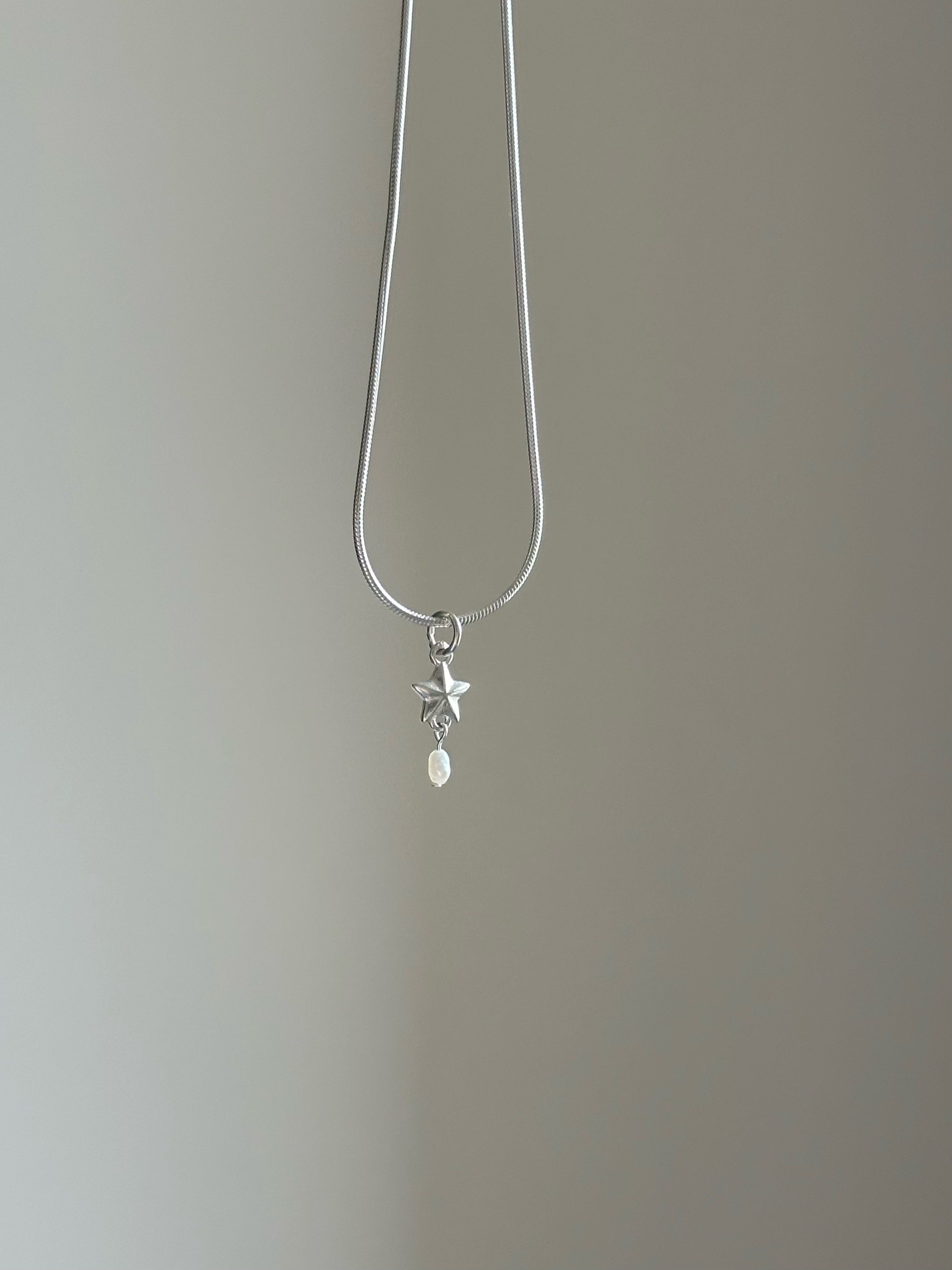 Silver necklace with a star and pearl pendant on a plain background