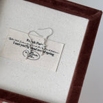Earring displayed on a card with text in a brown frame