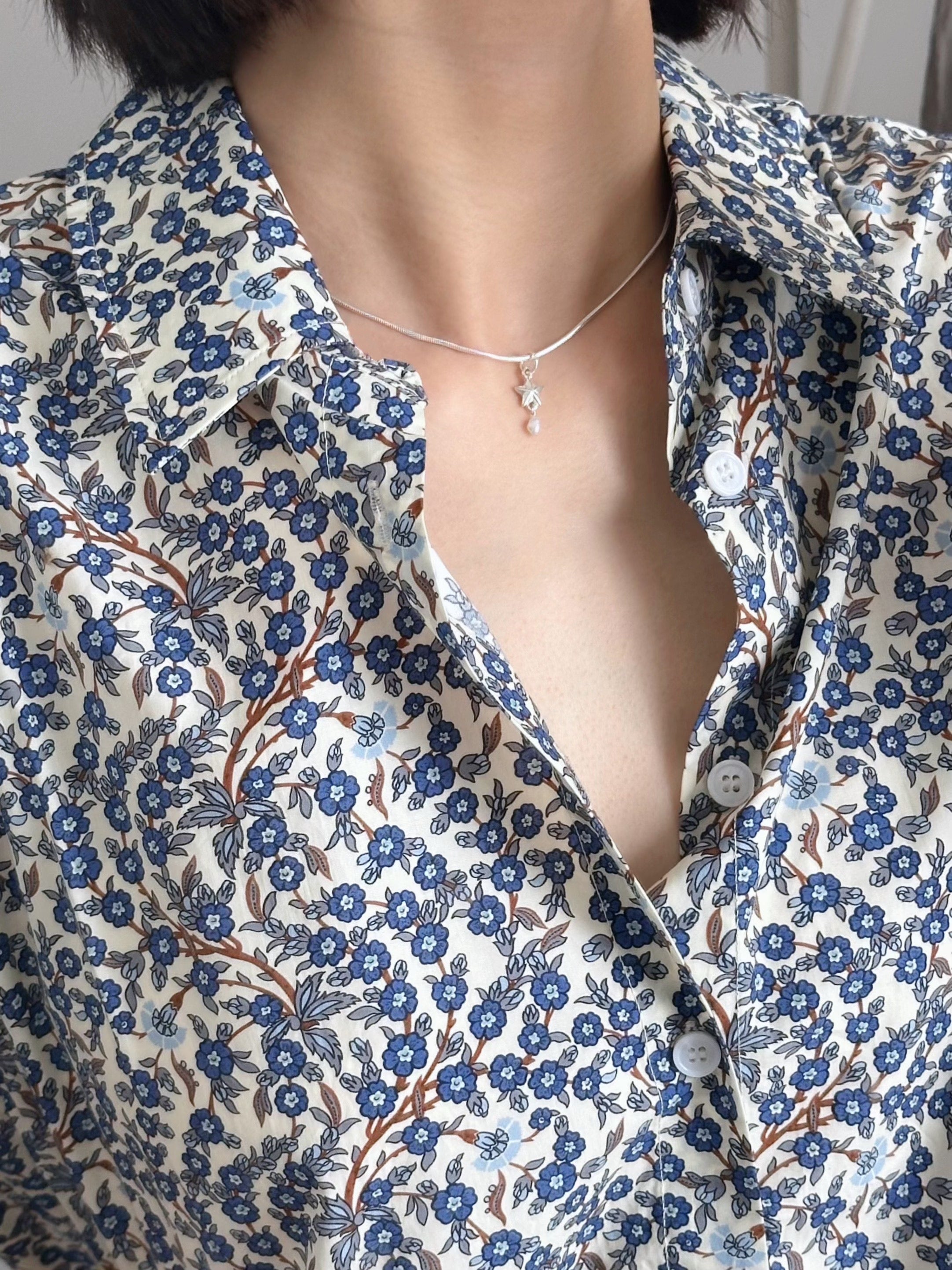 Floral patterned shirt with a deep neckline and necklace.