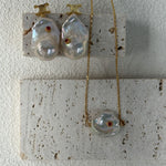 Pearl necklace and earrings on a textured surface with a white background