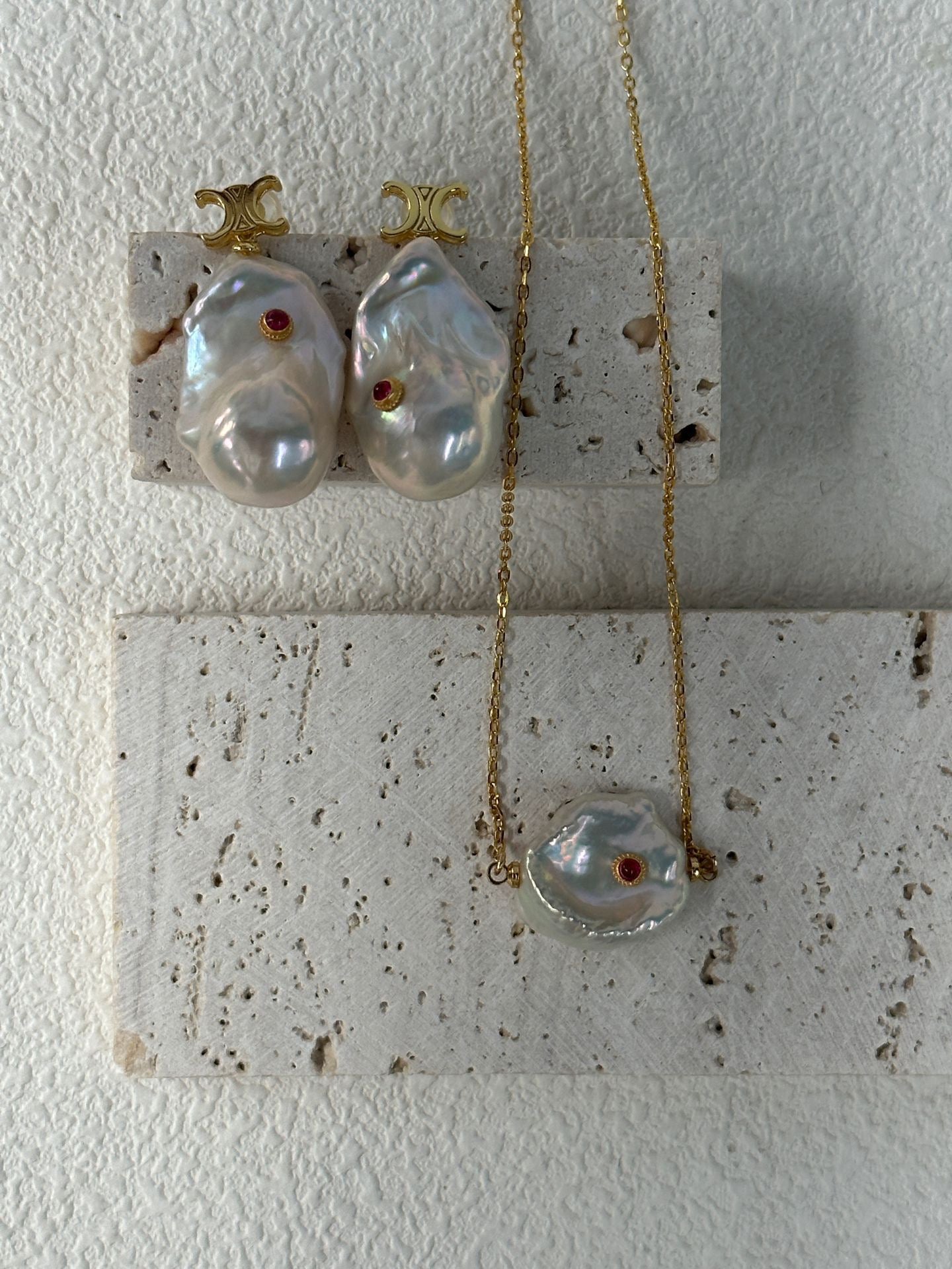Pearl necklace and earrings on a textured surface with a white background