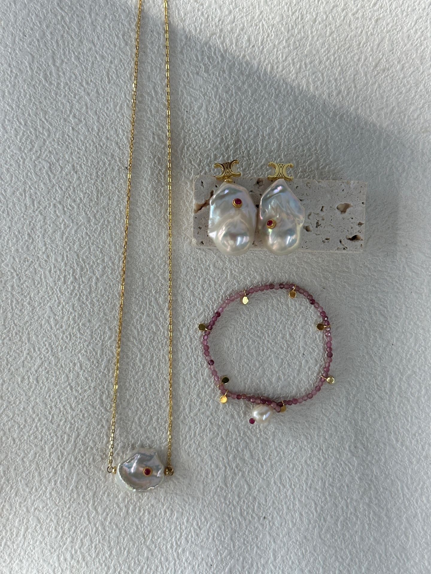 Jewelry set including a necklace, earrings, and bracelet on a textured white surface.