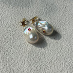 Pearl earrings with red gemstones on a light gray background