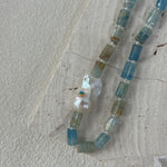 Necklace with blue and clear beads and a large pearl on a textured surface