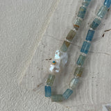 Necklace with blue and clear beads and a large pearl on a textured surface