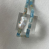 Necklace with blue beads and a large pearl-like bead on a white background