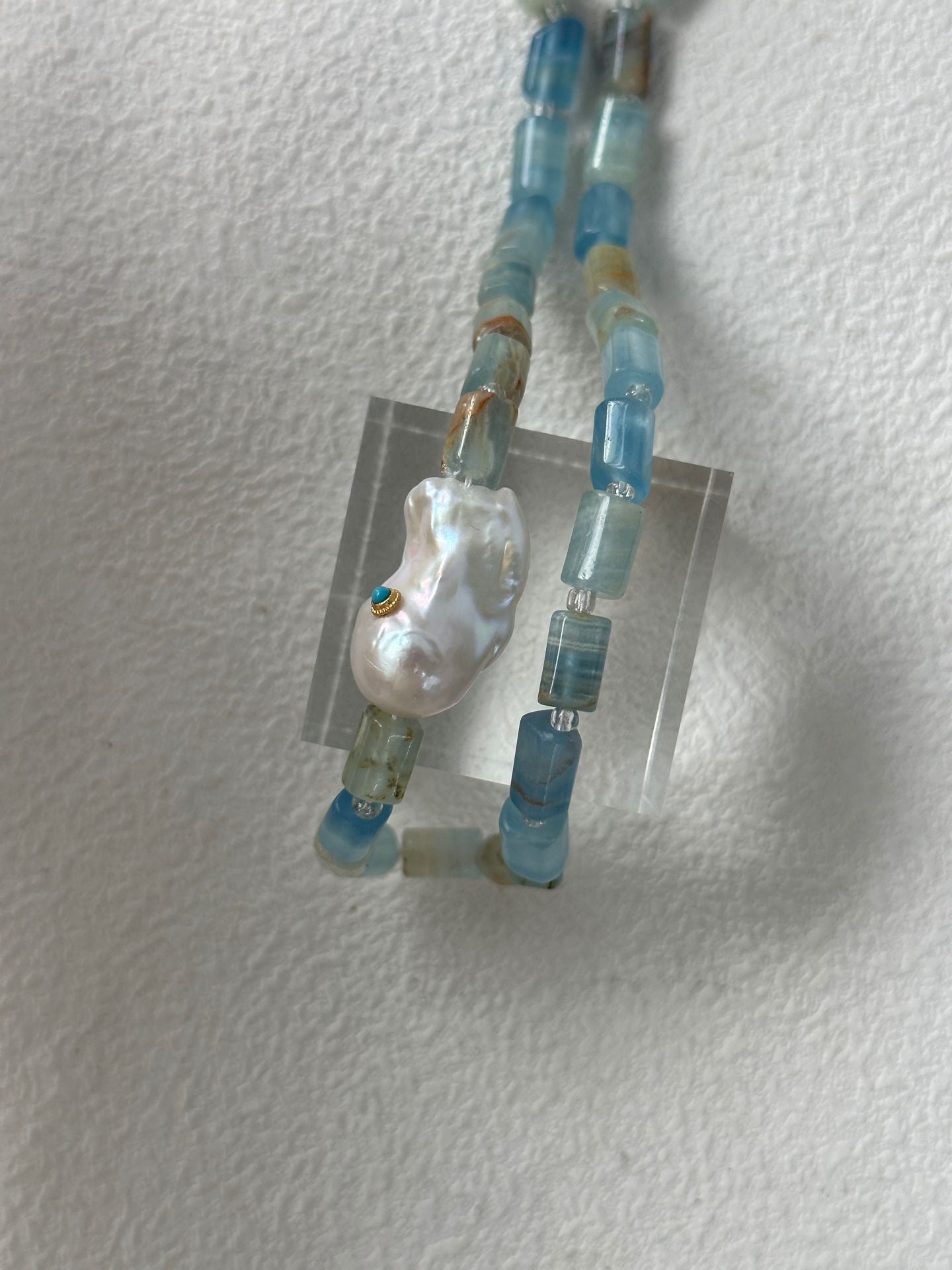 Necklace with blue beads and a large pearl-like bead on a white background