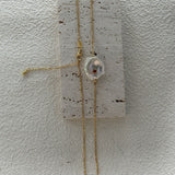Gold necklace with a pendant on a textured white surface