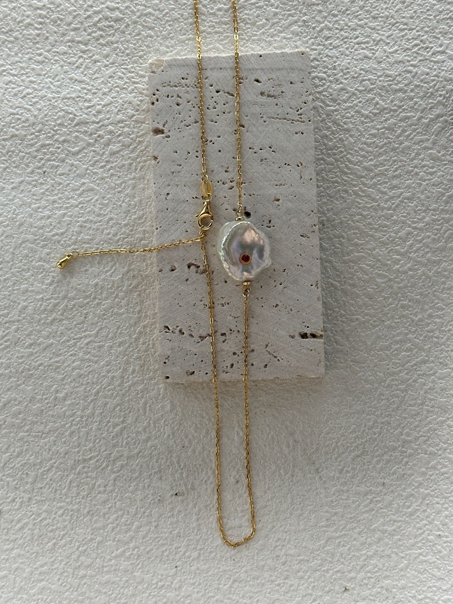 Gold necklace with a pendant on a textured white surface