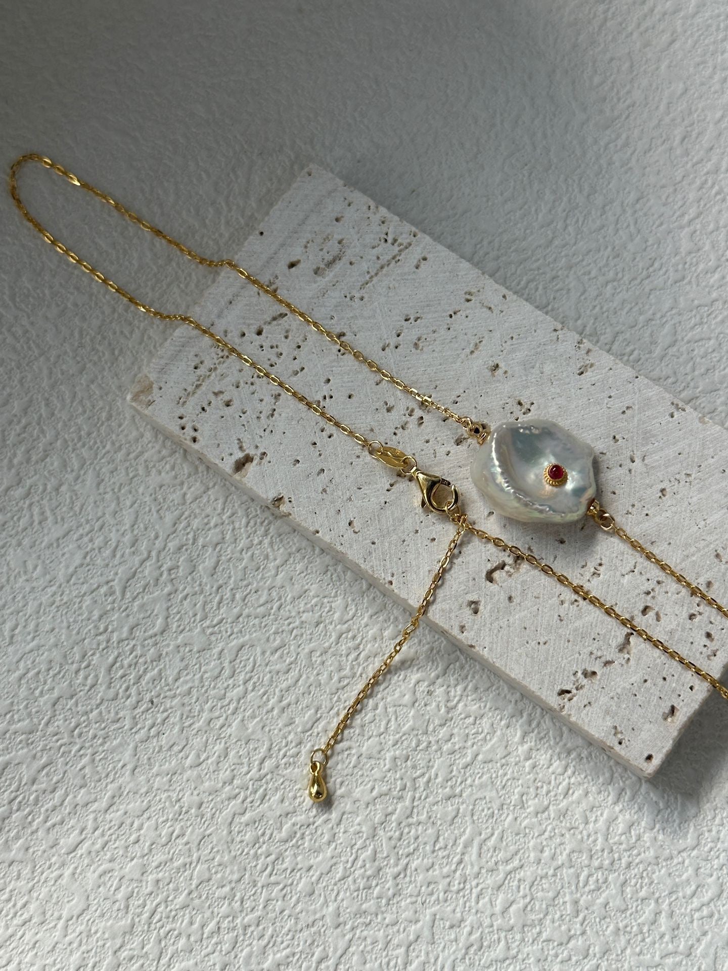 Gold necklace with a pendant on a textured white surface