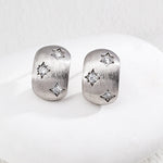 Pair of silver earrings with star designs on a white surface