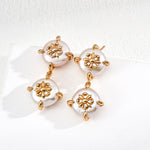 Pair of earrings with gold floral designs and pearl-like beads on a white background
