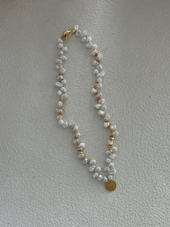 A keshi pearl necklace with gold plating and small gold accents, displayed on a beige surface.