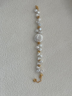 A bracelet with a combination of round pearls and gold-colored accents on a pale background.