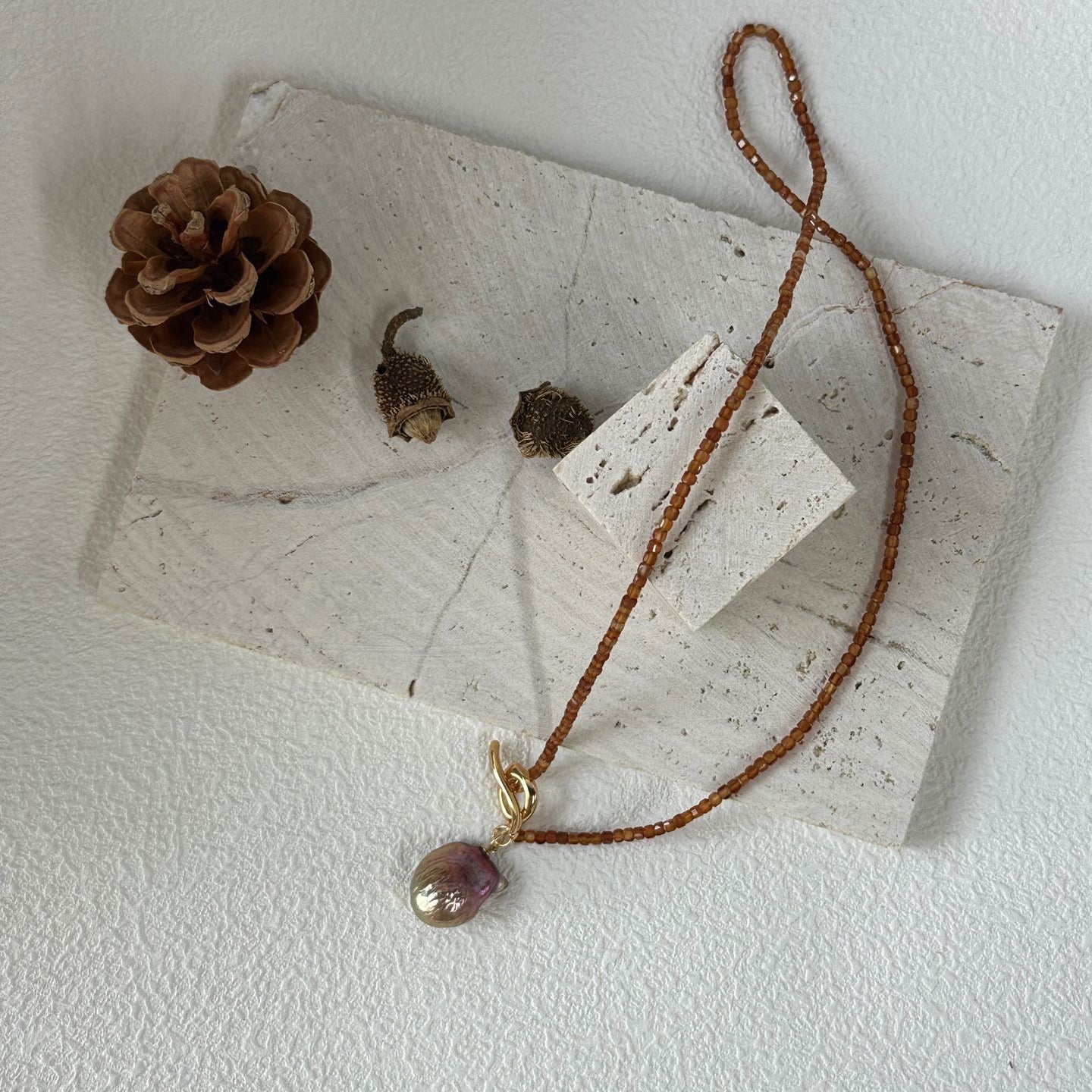 Necklace with a pendant on a white surface with a pine cone and leaves.