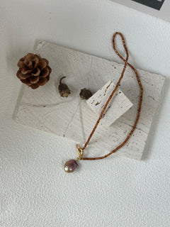 Necklace with a pendant on a white surface with a pine cone and leaves.