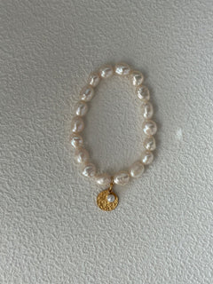 Pearl bracelet with a gold charm on a light gray background