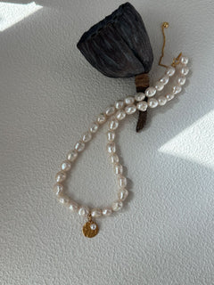 Pearl bracelet with a gold charm on a white surface