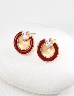 Pair of earrings with gold and red circular design on a white cushion