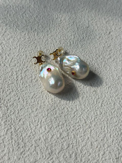 Pearl earrings with red gemstones on a light gray background