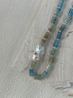 Necklace with blue and clear beads and a large pearl on a textured surface