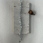 Decorative hanging wall art with beads and a small pine cone on a plain white background