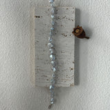 Decorative hanging wall art with beads and a small pine cone on a plain white background