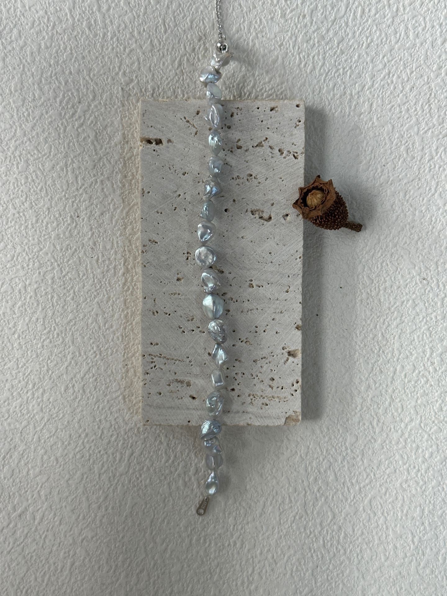 Decorative hanging wall art with beads and a small pine cone on a plain white background