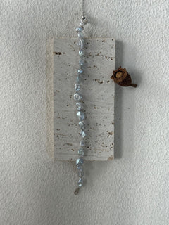 Decorative hanging wall art with beads and a small pine cone on a plain white background