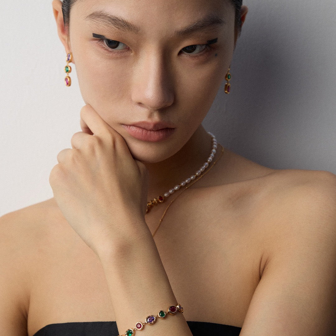 Woman wearing a necklace and bracelet with gemstones against a neutral background