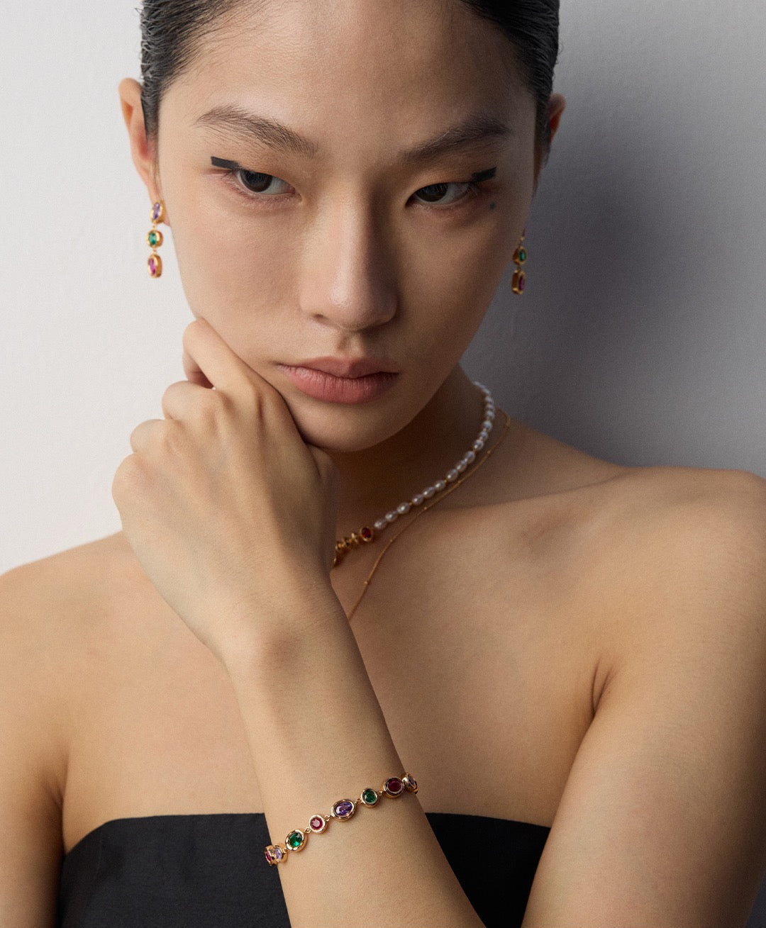 Woman wearing a necklace and bracelet with gemstones against a neutral background