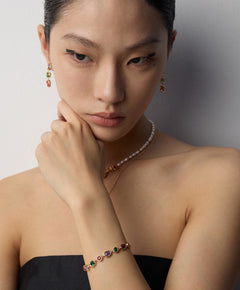 Woman wearing a necklace and bracelet with gemstones against a neutral background