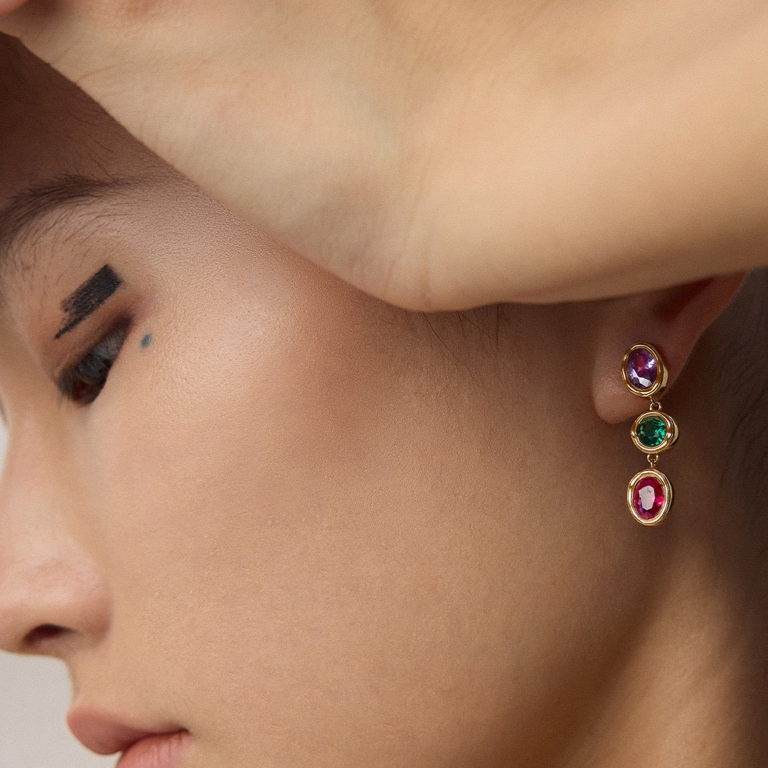 Close-up of a person wearing colorful gemstone earrings.