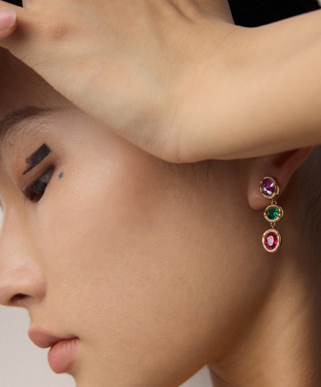 Close-up of a person wearing colorful gemstone earrings.