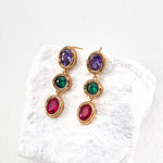 Gold earrings with multicolored gemstones on a white textured surface