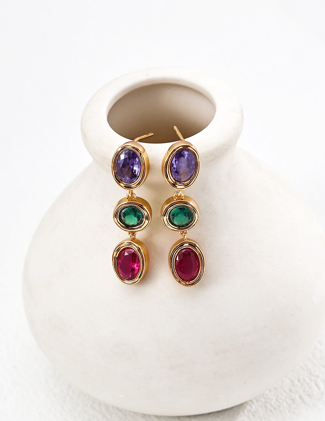 Colorful gemstone earrings on a white ceramic vase