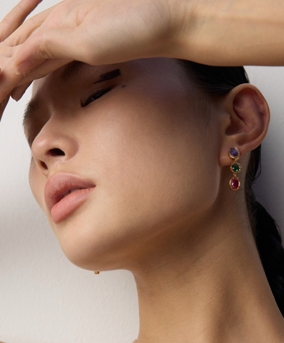 Close-up of a person wearing colorful earrings with a neutral background