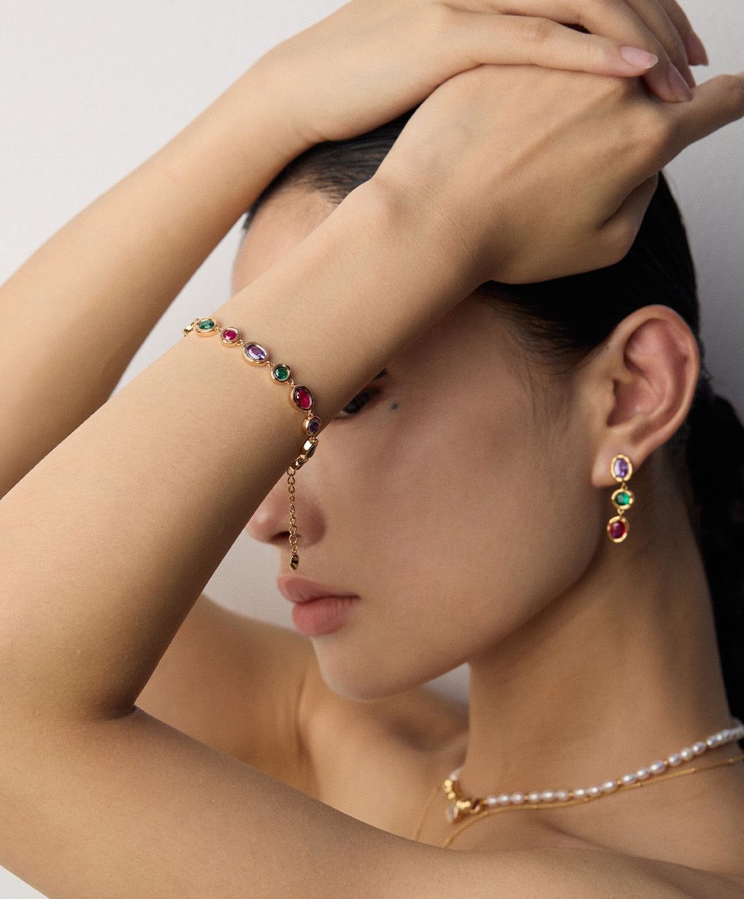 Woman wearing a colorful gemstone bracelet and earrings with a neutral background