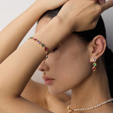 Woman wearing a colorful gemstone bracelet and earrings with a neutral background