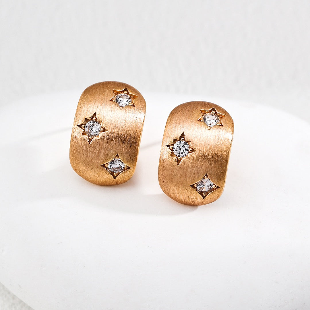 Rose gold earrings with star-shaped gemstones on a white background