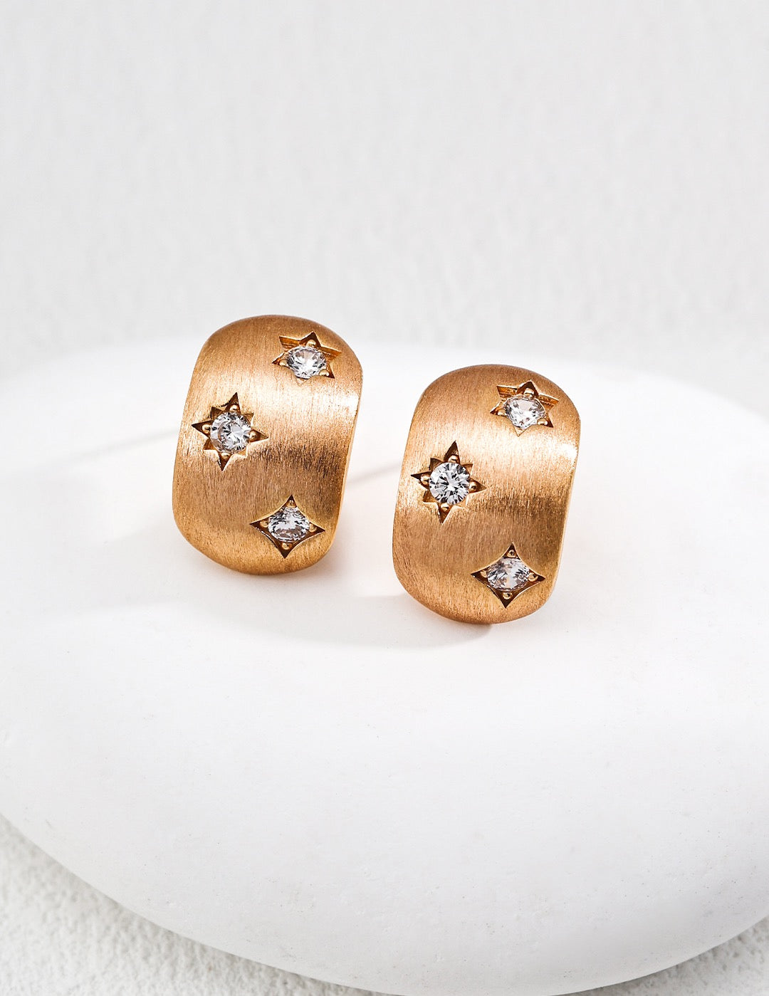 Rose gold earrings with star-shaped gemstones on a white background
