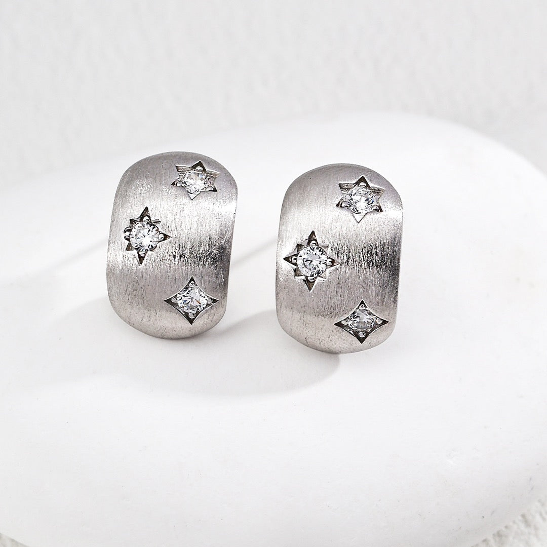 Pair of silver earrings with star designs on a white surface