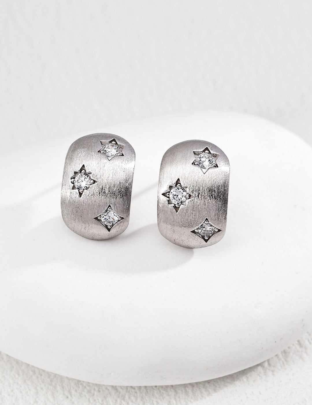 Pair of silver earrings with star designs on a white surface