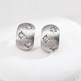 Pair of silver earrings with star designs on a white surface
