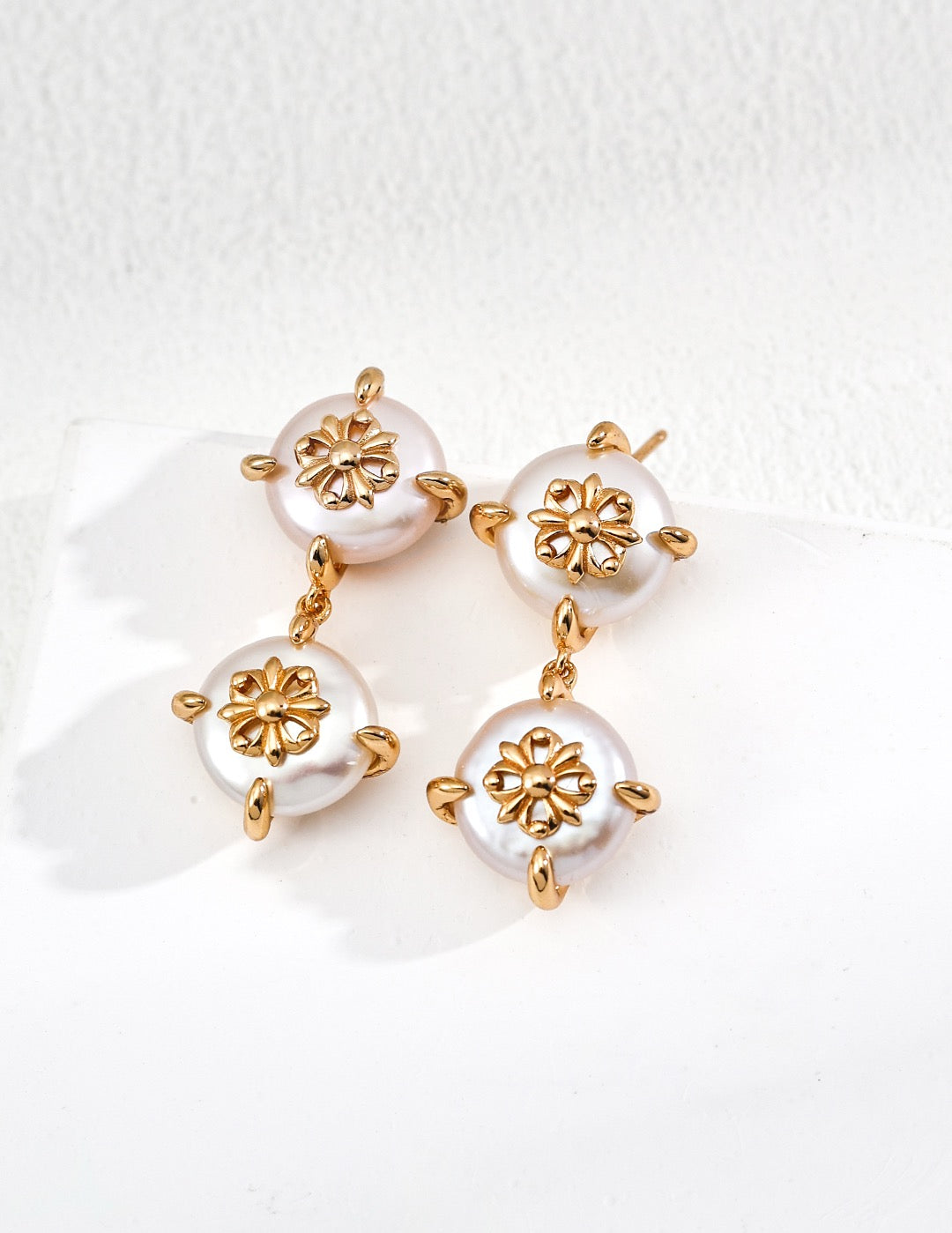 Pair of earrings with gold floral designs and pearl-like beads on a white background
