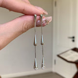 Silver teardrop earrings held by a hand with a neutral background