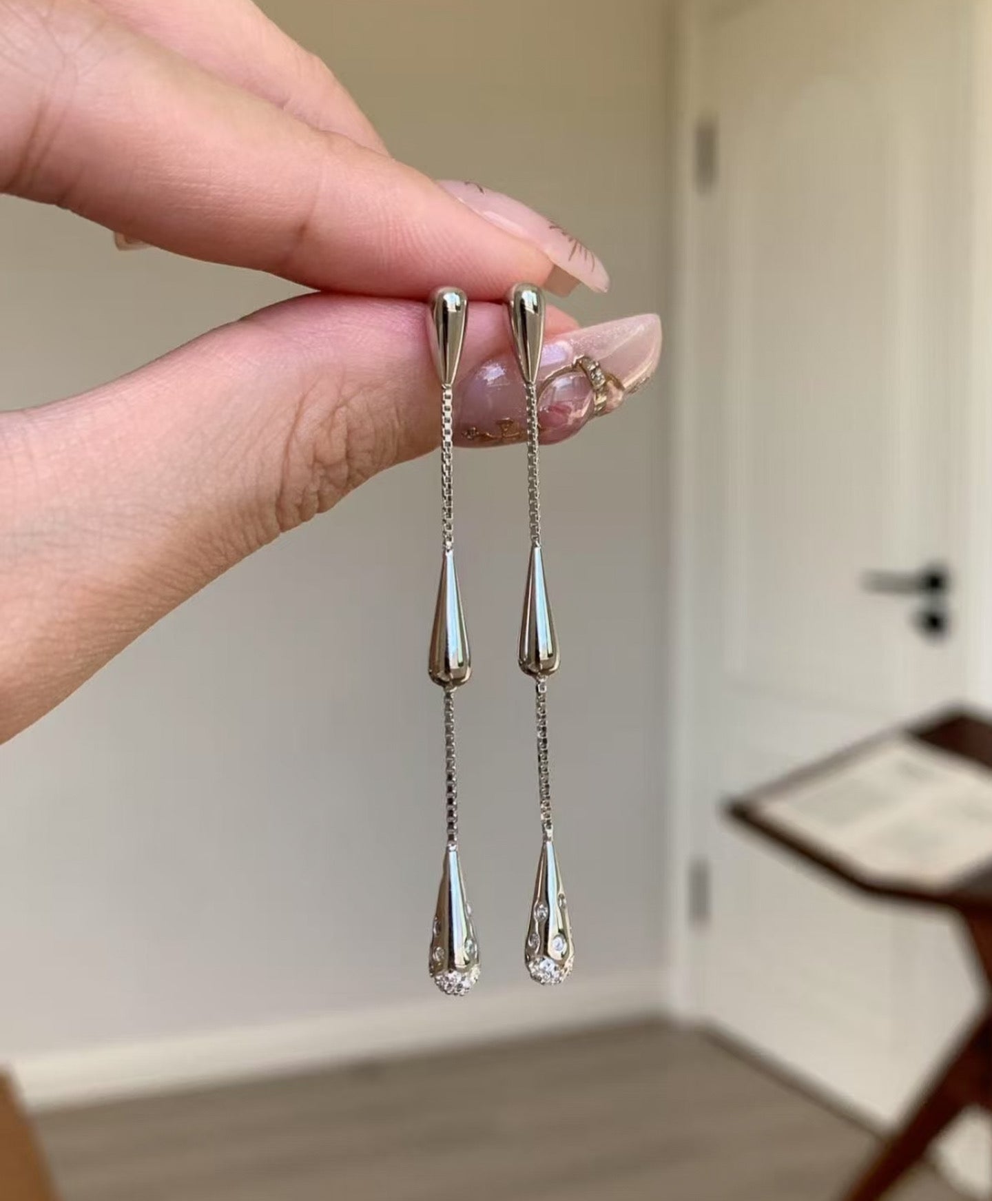 Silver teardrop earrings held by a hand with a neutral background