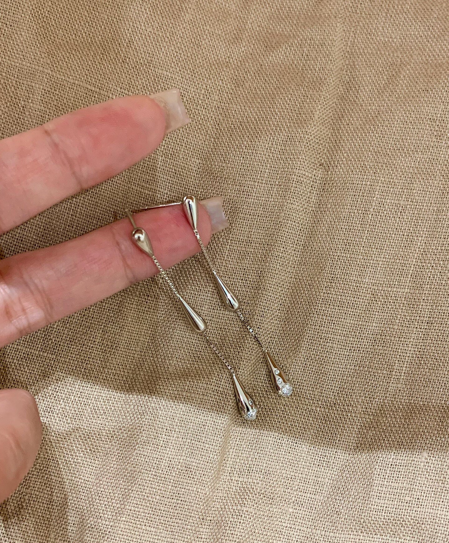 Silver hairpins held between fingers on a beige fabric background 
